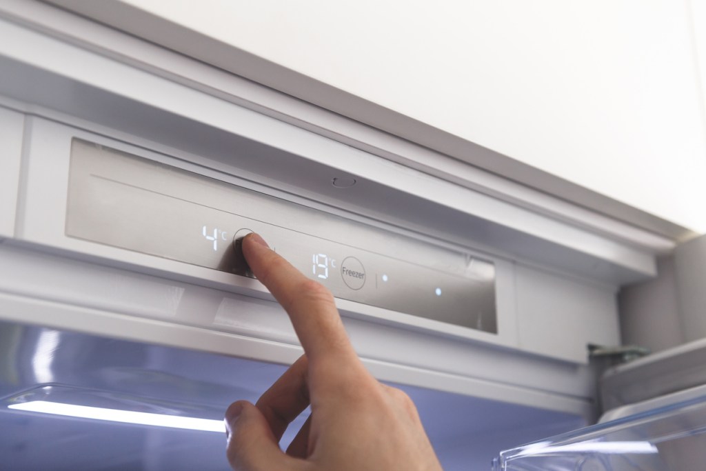 Hand adjusts temperature of refrigerator. Choosing a refrigerator operating mode, setting the correct temperature